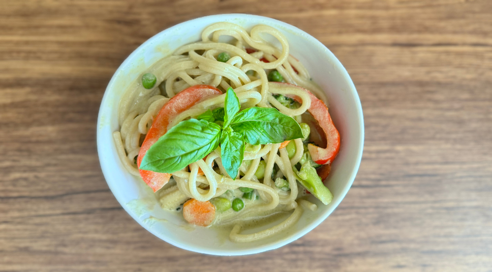 Thai green curry pasta served in a bowl, coated in creamy green curry sauce, garnished with fresh herbs and vegetables.